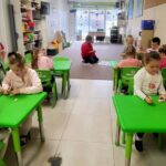 na zdjęciu widać dzieci siedzące przy zielonych stolikach