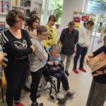 W pomieszczeniu czytelni stoi drupa osób. Jedna z pań prezentuje książkę. Reszta przygląda się.