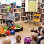 na zdjęciu widać kobietę pokazująca dzieciom pluszowe owoce