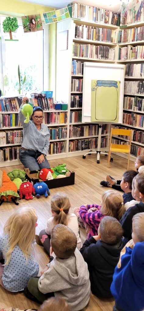 na zdjęciu widać kobietę pokazująca dzieciom pluszowe owoce