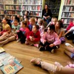 na zdjęciu widać dzieci w sali bibliotecznej, siedzące na podłodze a przed nimi książki
