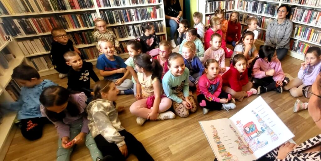 na zdjęciu widać dzieci w sali bibliotecznej siedzące na podłodze
