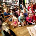 na zdjęciu widać dzieci w sali bibliotecznej siedzące na podłodze