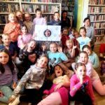 na zdjęciu widać dzieci w sali bibliotecznej siedzące na podłodze