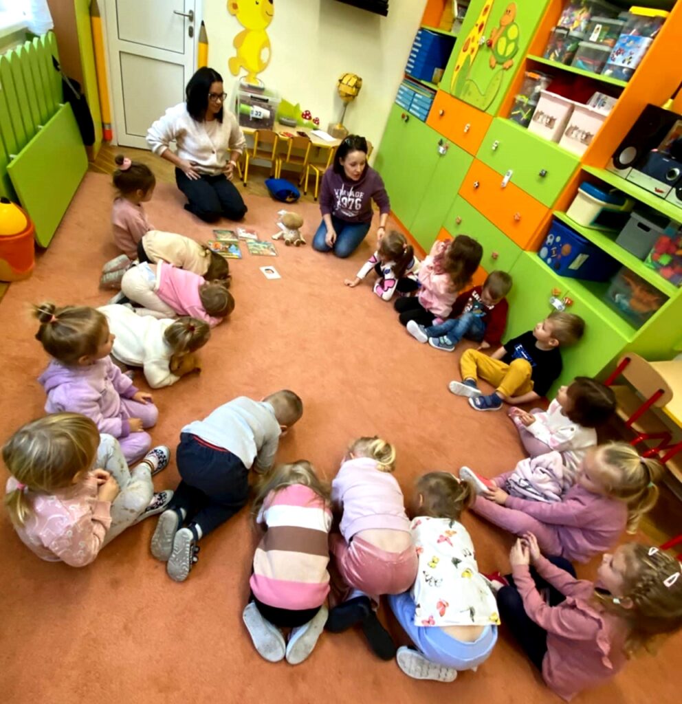 na zdjęciu widać dzieci siedzące na podłodze w sali przedszkolnej