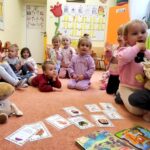 na zdjęciu widać dzieci siedzące na podłodze w sali przedszkolnej a przed nimi kolorowe książeczki