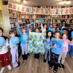 na zdjęciu widać dzieci w sali bibliotecznej trzymające rysunki
