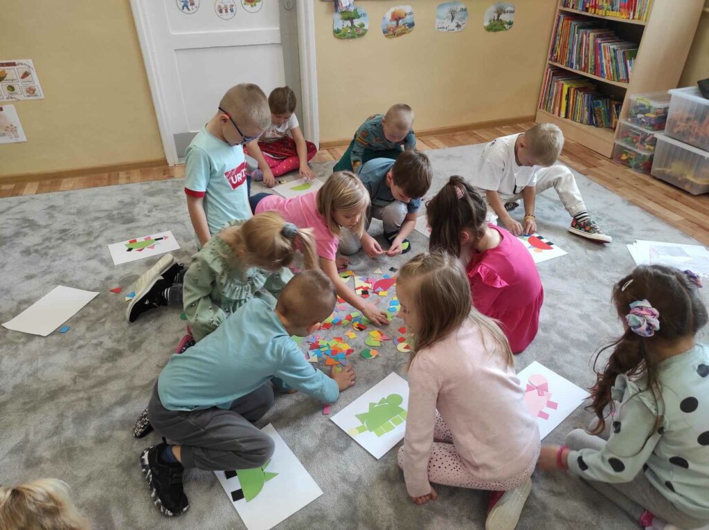 na zdjęciu widać salę przedszkolną, na dywanie siedzą dzieci, biorą udział w zabawie