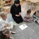 na zdjęciu widać salę przedszkolną, na dywanie siedzą dzieci, biorą udział w zabawie