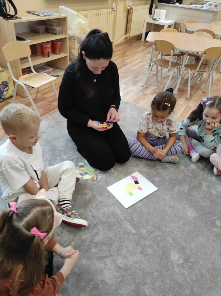 na zdjęciu widać salę przedszkolną, na dywanie siedzą dzieci, biorą udział w zabawie