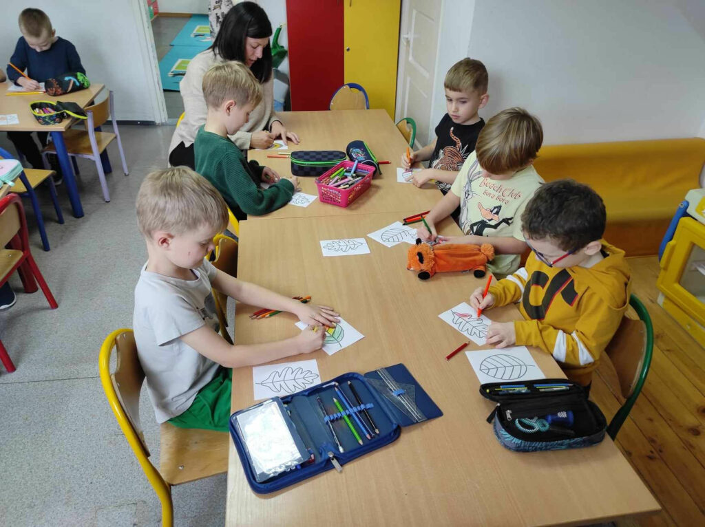na zdjęciu widać salę przedszkolną, dzieci siedzą przy stolikach, kolorują liście