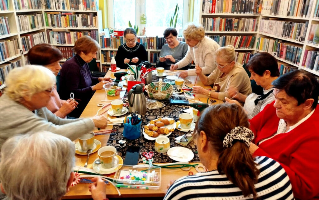 na zdjęciu widać seniorki siedzące wokół stołu w sali bibliotecznej i wykonujące ozdoby świąteczne
