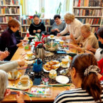na zdjęciu widać seniorki siedzące wokół stołu w sali bibliotecznej i wykonujące ozdoby świąteczne