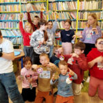 na zdjęciu widać dzieci w sali bibliotecznej pozujące na tle regałów z książkami