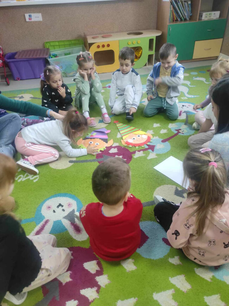 na zdjęciu widać salę przedszkolną, na dywanie siedzą dzieci, biorą udział w zabawie