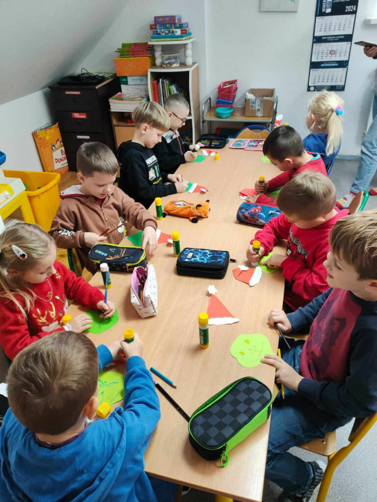 na zdjęciu widać salę przedszkolną, przy stolikach siedzą dzieci, wykonują pracę plastyczną