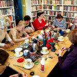 na zdjęciu widać seniorki siedzące wokół stołu w sali bibliotecznej i wykonujące ozdoby świąteczne