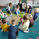 na zdjęciu widać salę przedszkolną, dzieci siedzą na dywanie, biorą udział w zabawie