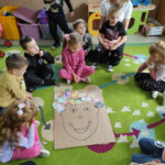 na zdjęciu widać salę przedszkolną, dzieci siedzą na dywanie, biorą udział w zabawie
