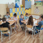 na zdjęciu widać salę przedszkolną, dzieci siedzą przy stolikach, wykonują pracę plastyczną