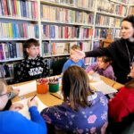 na zdjęciu widać dzieci siedzące wokół stołu w sali bibliotecznej