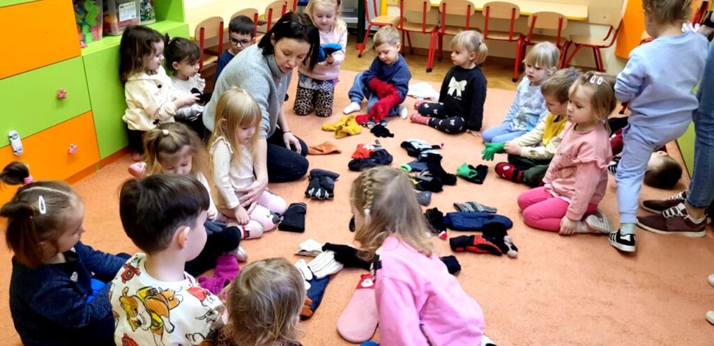 na zdjęciu widać dzieci siedzące na podłodze a wokół nich rozsypane rękawiczki