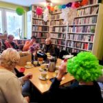 na zdjęciu widać seniorki siedzące wokół stołu w sali bibliotecznej