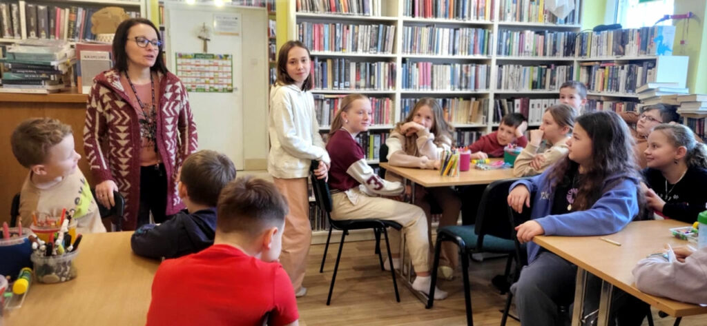 na zdjęciu widać dzieci siedzące przy stołach w sali bibliotecznej