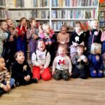 na zdjęciu widać dzieci w sali bibliotecznej stojące na tle regałów z książkami