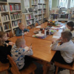 na zdjęciu widać salę biblioteczną, przy stole siedzą dzieci, biorą udział w zabawie