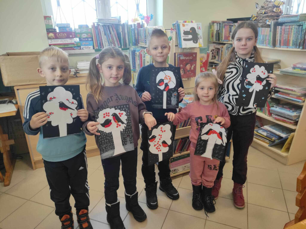 na zdjęciu widać salę biblioteczną, dzieci prezentują wykonane prace plastyczne z poważaniem