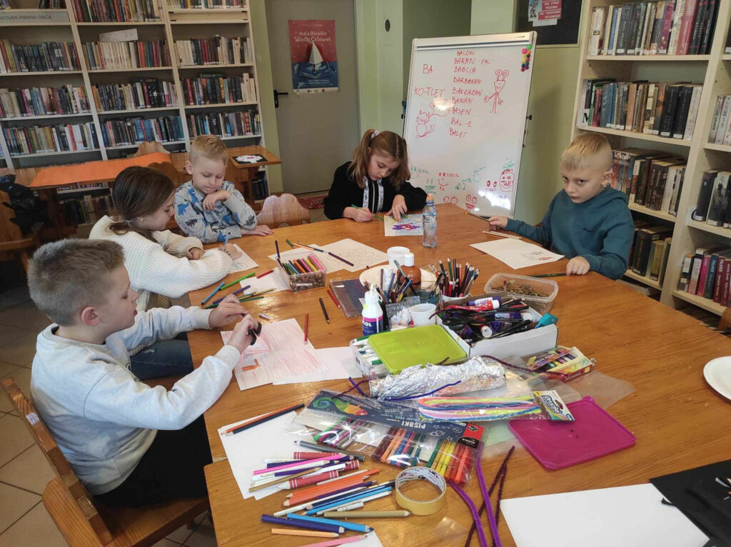 na zdjęciu widać salę biblioteczną, przy stole siedzą dzieci, tworzą komiks