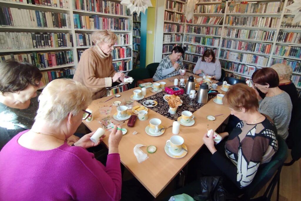 na zdjęciu widać seniorki siedzące wokół stołu w sali bibliotecznej