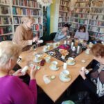 na zdjęciu widać seniorki siedzące wokół stołu w sali bibliotecznej