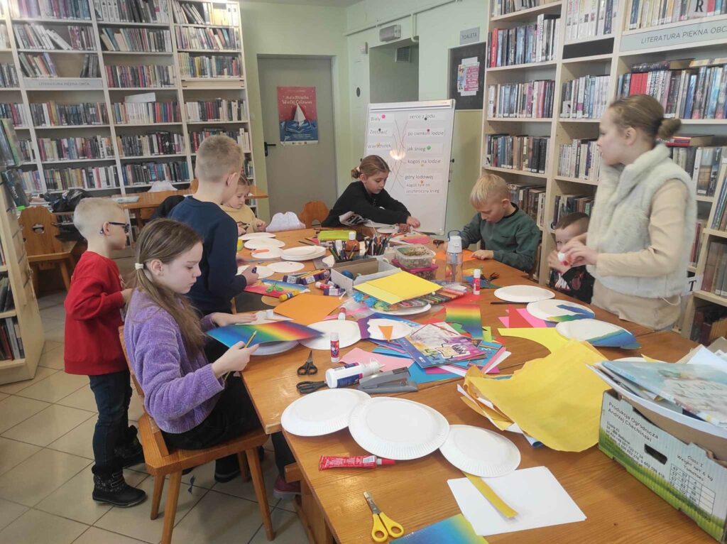 na zdjęciu widać salę biblioteczną, dzieci siedzą przy stole, wykonują pracę plastyczną