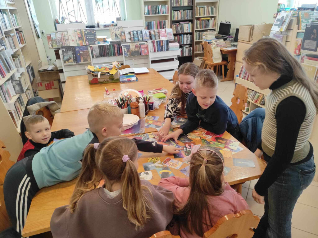 na zdjęciu widać salę biblioteczną, dzieci siedzą przy stole, biorą udział w zabawie