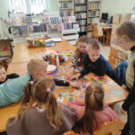 na zdjęciu widać salę biblioteczną, dzieci siedzą przy stole, biorą udział w zabawie
