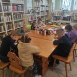 na zdjęciu widać salę biblioteczną, dzieci siedzą przy stole, rozwiązują zadanie