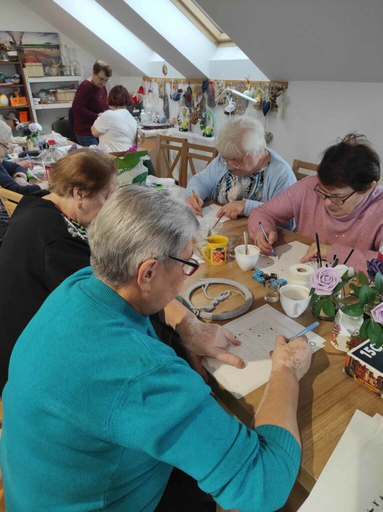 na zdjęciu widać seniorów siedzących przy stole, rozwiązują zadania
