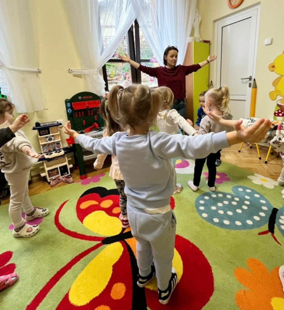 na zdjęciu widać salę przedszkolną i dzieci oraz pania bibliotekarkę. Wszyscy uczestniczą w zabawie