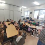 Przy stołach siedzą dwadzieścia pięć dzieci w wieku szkolnym. Pani bibliotekarka czyta im książkę a dzieci słuchają.