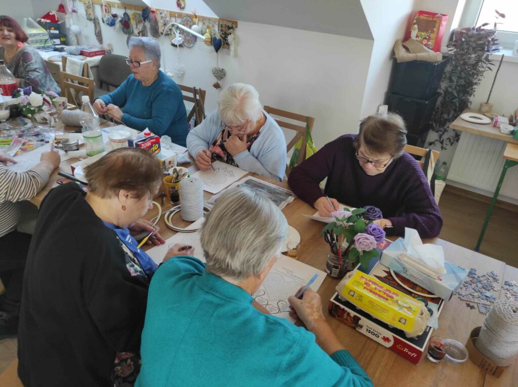 na zdjęciu widać seniorów siedzących przy stole, rozwiązują zadania