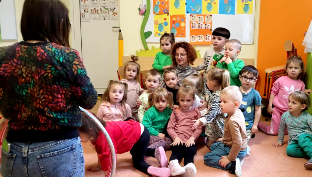 na zdjęciu widać dzieci w sali przedszkolnej siedzące na ziemi