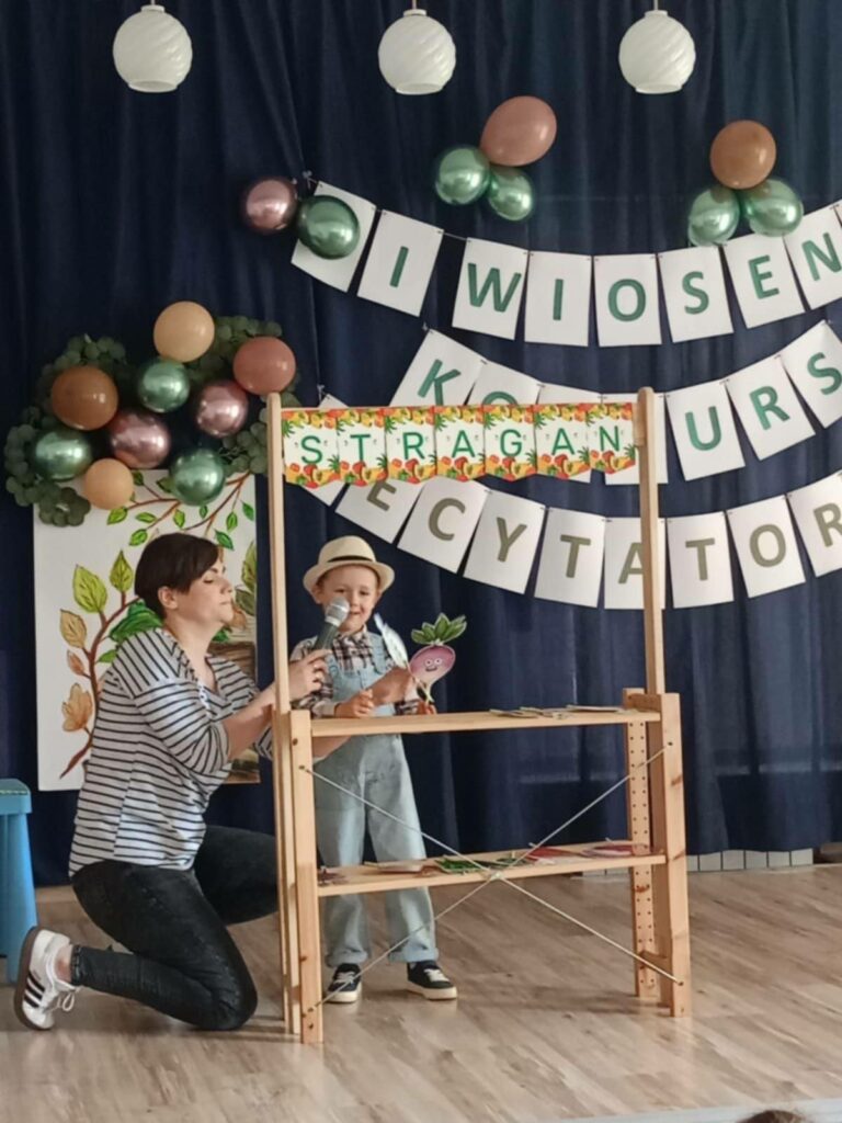 Na zdjęciu chłopiec, który recytuje wiersz. Pani trzyma mikrofon.