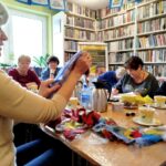 na zdjęciu widać kobiety wokół stołu w sali bibliotecznej a przed nimi kolorowa wełna
