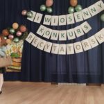 Na zdjęciu widać dziewczynkę w wieku około 10 lat trzyma w ręku mikrofon w tyle napis Wiosenny Konkurs Recytatorski.