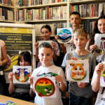 na zdjęciu widać młodzież stojącą w sali bibliotecznej i trzymającą prace plastyczne. Obrazki z filcu