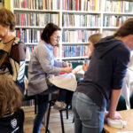 na widać osoby w różnym wieku dzieci i seniorki stojące w sali bibliotecznej
