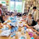 na zdjęciu widać osoby siedzące wokół stołu w sali bibliotecznej i wykonujące obrazy z filcu
