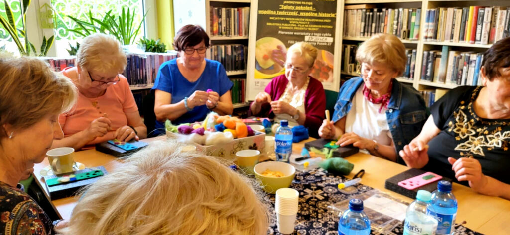 na zdjęciu widać seniorki siedzące wokół stołu w sali bibliotecznej